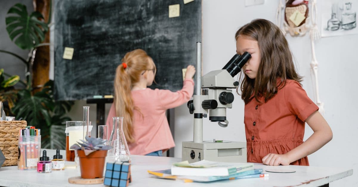 Two girls engaged in a science experiment using a microscope in a classroom setting.