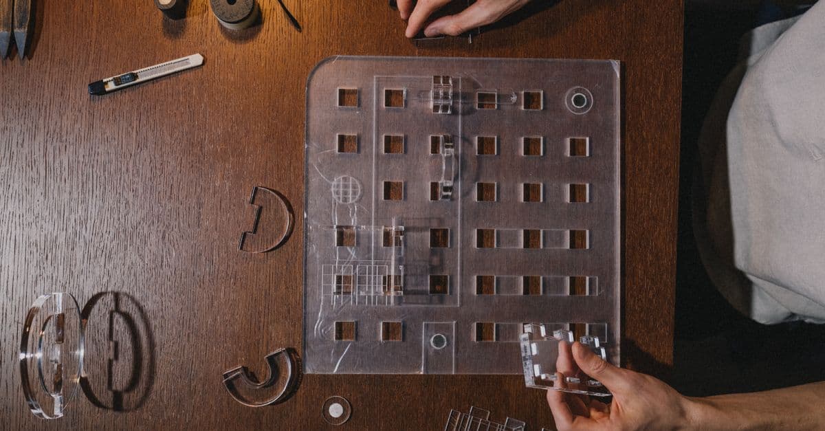 Hands assembling an architectural model with tools on a wooden table, showcasing precision and creativity.