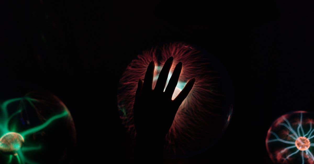 Silhouette of a hand interacting with a glowing plasma ball, illustrating electric waves.