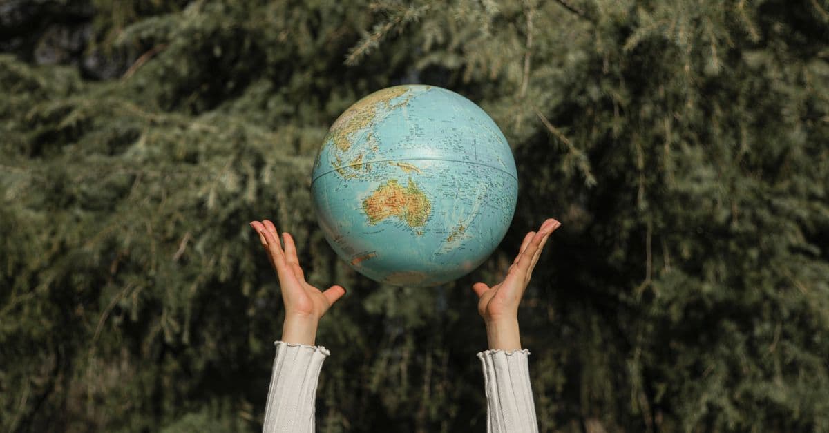 Hands raising a globe against a lush green tree backdrop, symbolizing environmental awareness.