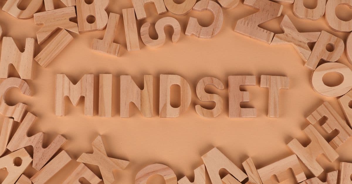 Wooden alphabet letters arranged to spell 'Mindset' on a peach background.