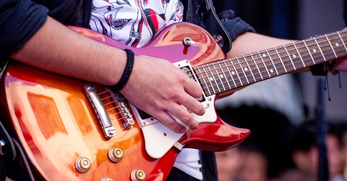 Vibrant close-up of a guitarist performing with a red electric guitar at an outdoor event.