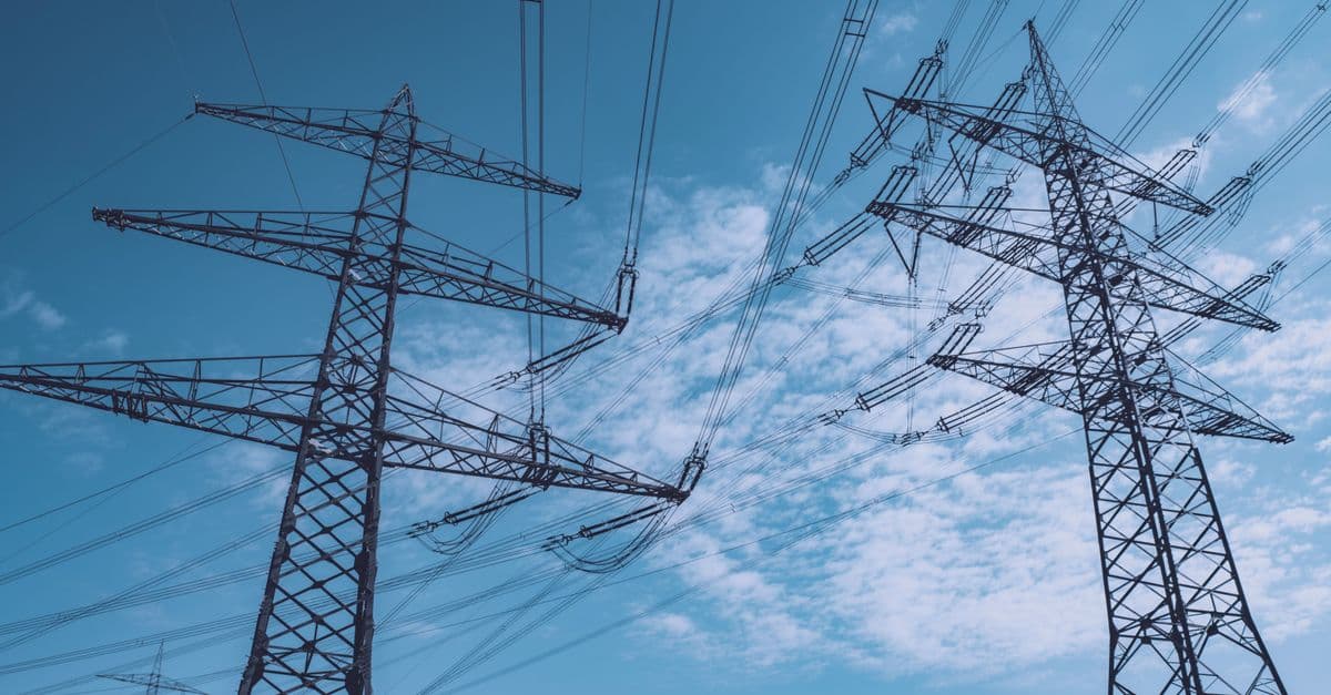 High voltage transmission towers stretch across a clear blue sky, symbolizing energy and industry.