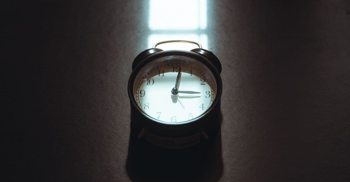 A vintage alarm clock in cozy morning light casting artistic shadows on a desk.