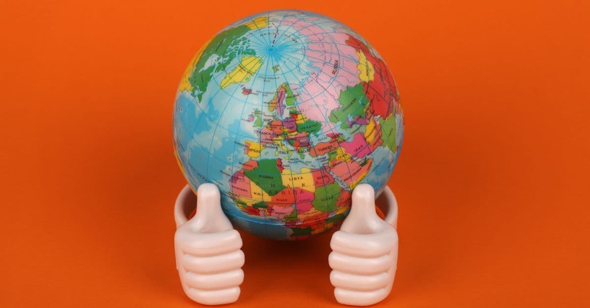 Vibrant globe model with thumbs-up figurines on orange background, symbolizing global positivity.