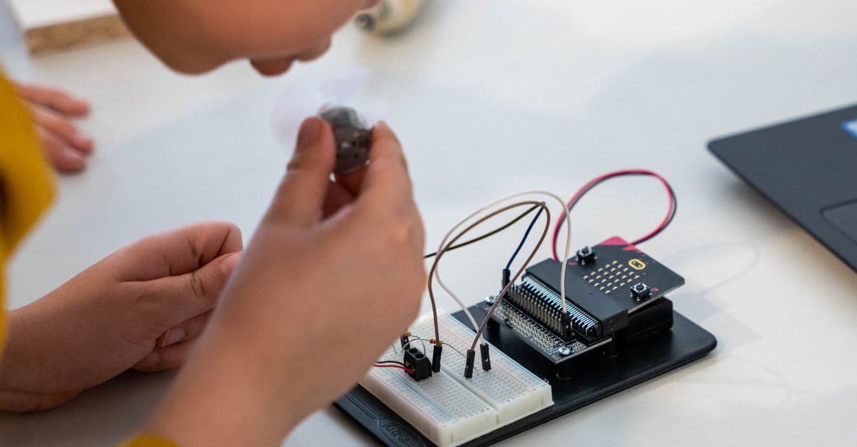 Young child assembling an electronic circuit with a microcontroller on a workbench.