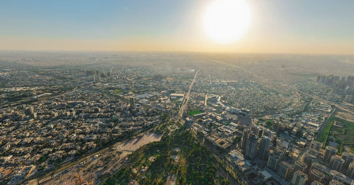 Panoramic aerial view of a sprawling cityscape under a bright sunset sky.