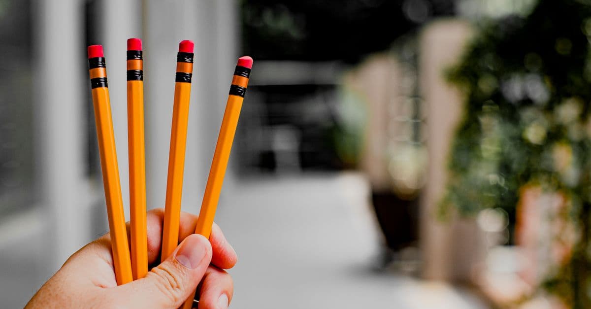 A hand holding four yellow pencils with erasers, perfect for educational and creative themes.