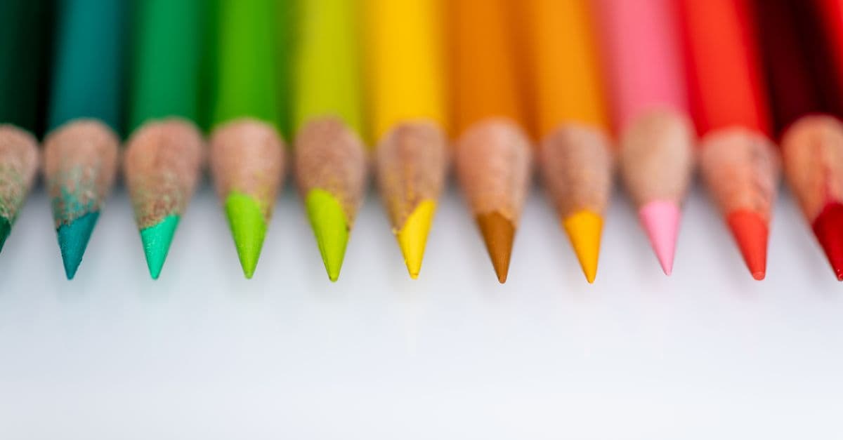 Collection of multicolored sharp wooden pencils for drawing arranged in row on white table in light room on blurred background