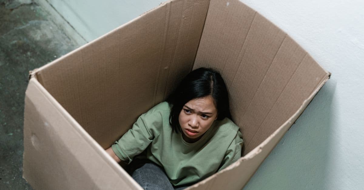 Woman in a cardboard box, symbolizing feelings of anxiety and claustrophobia.