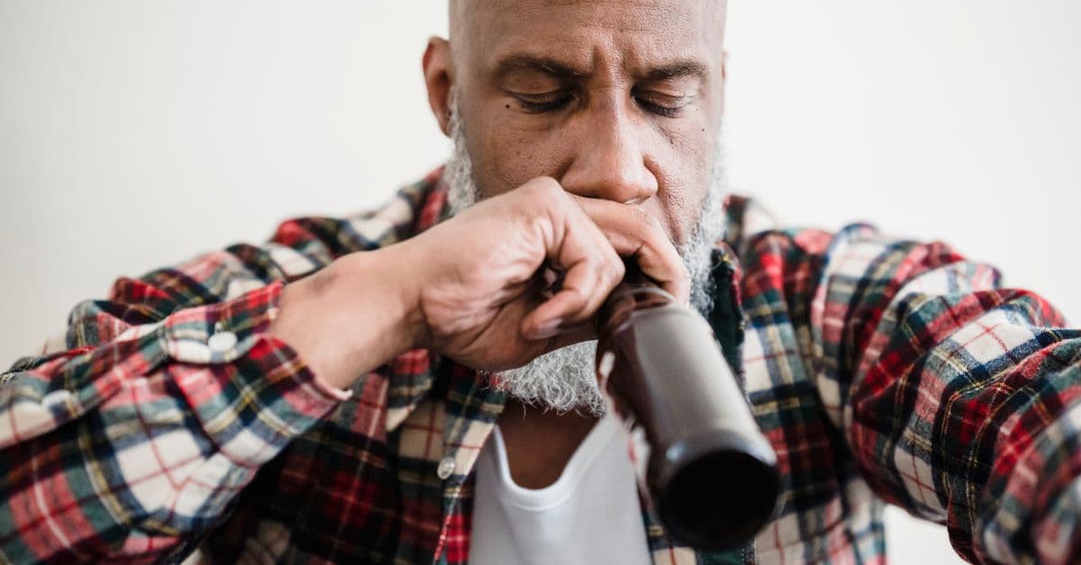 Adult man sitting indoors looking pensive with a beer bottle, conveying emotions of stress or contemplation.