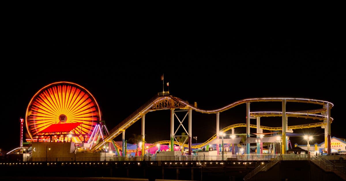 Brightly lit Santa Monica Pier with ferris wheel and roller coaster at night.