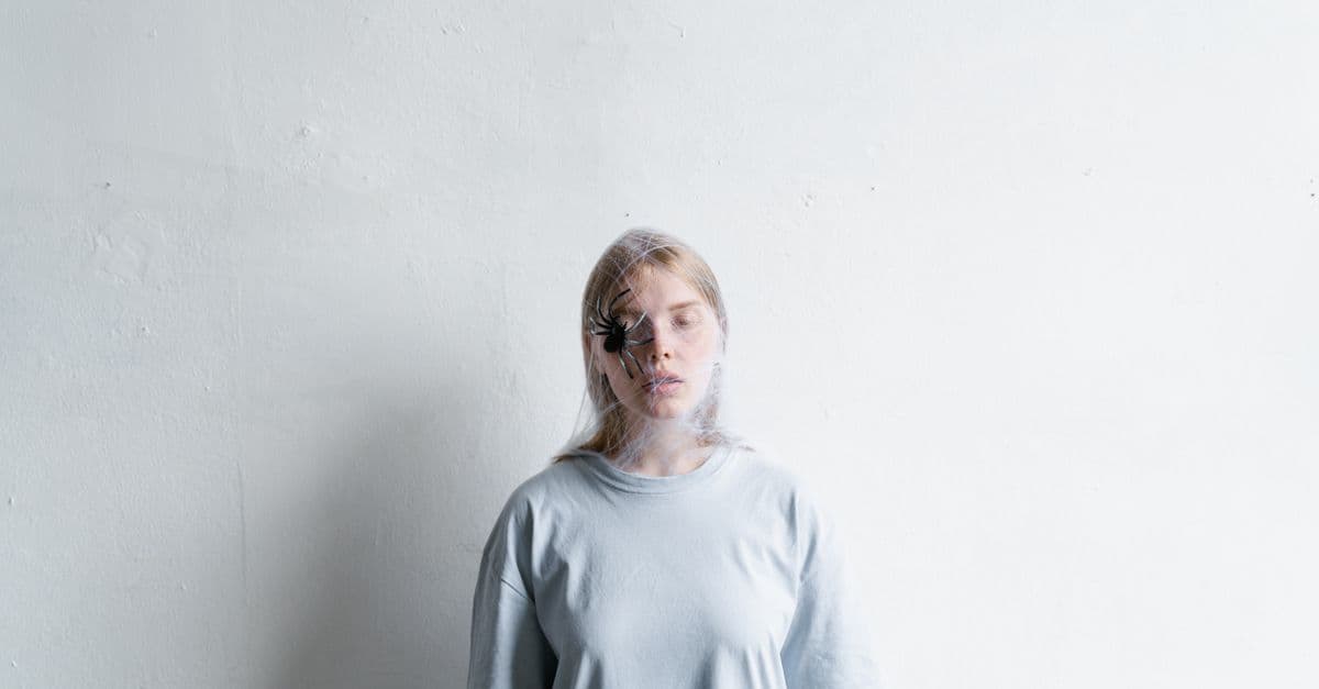 A young woman with a spider on her face symbolizes anxiety and fear against a white background.