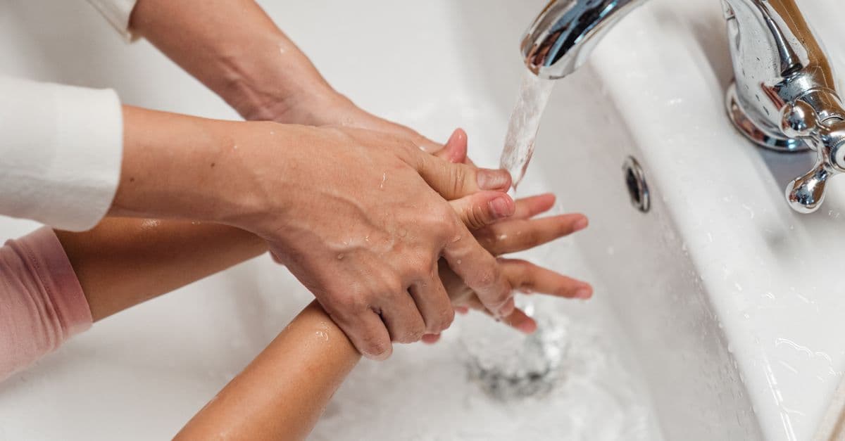 From above of crop anonymous mother washing hands of child in large ceramic washbasin