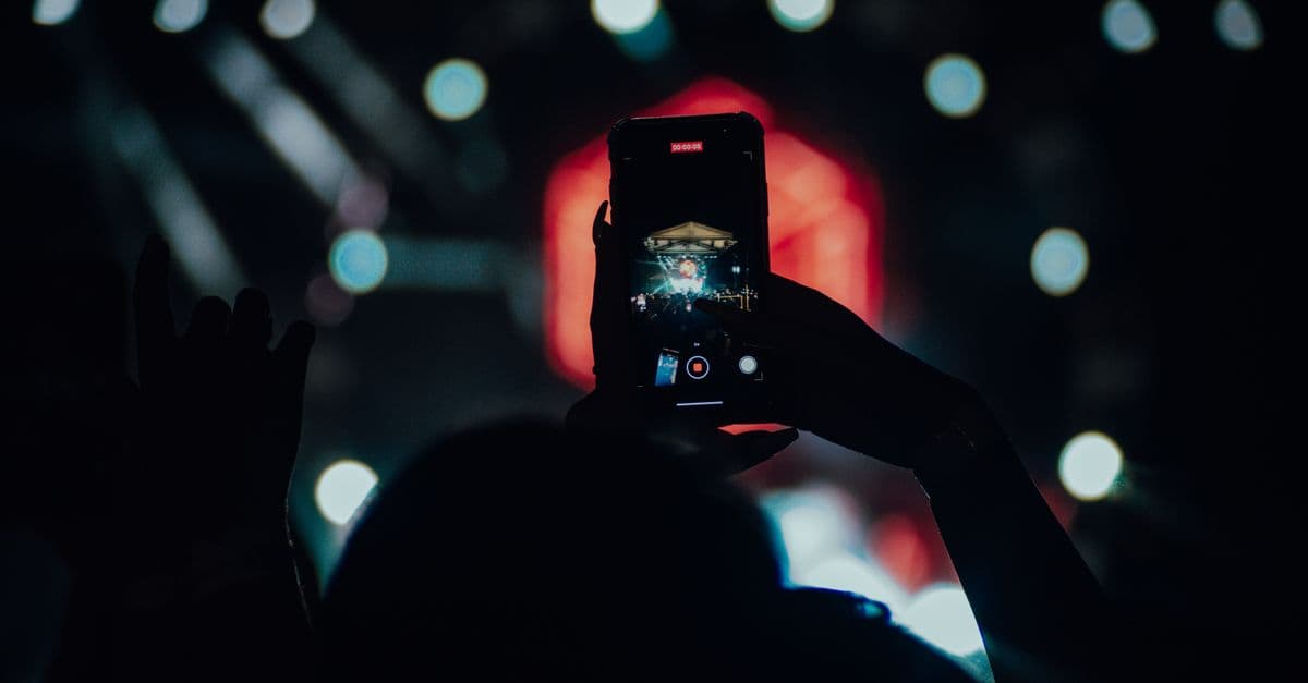 Silhouette using a smartphone to record a live concert scene.