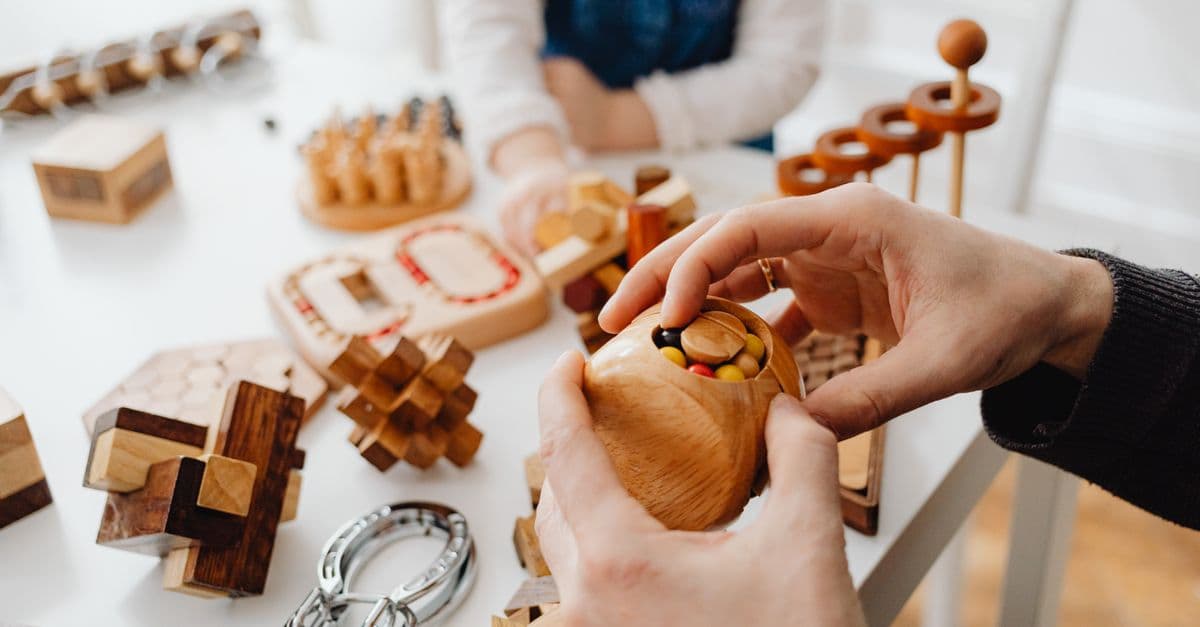 Close-up of hands engaging with wooden brain teasers on a table indoors.