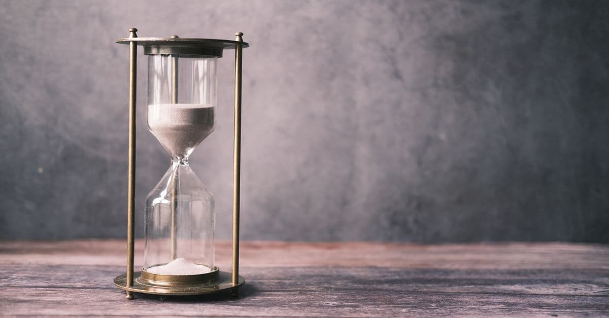 A classic hourglass with sand on a rustic wooden table against a soft gray background, offering ample copy space.