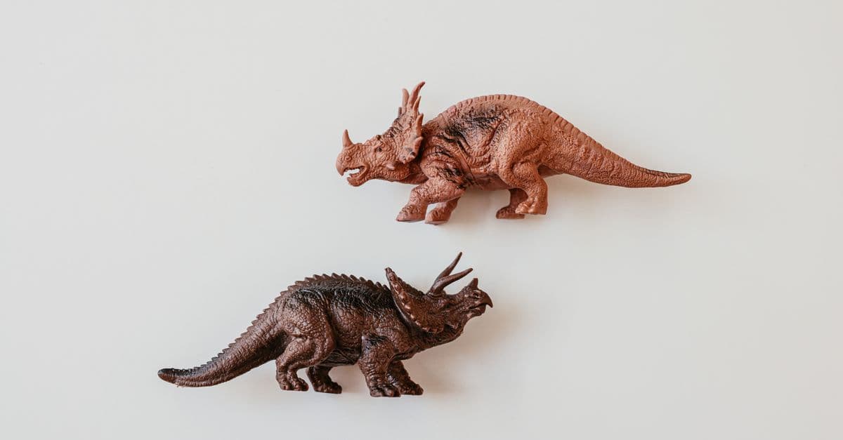 Two detailed dinosaur toy models, including a Triceratops, on a white surface.
