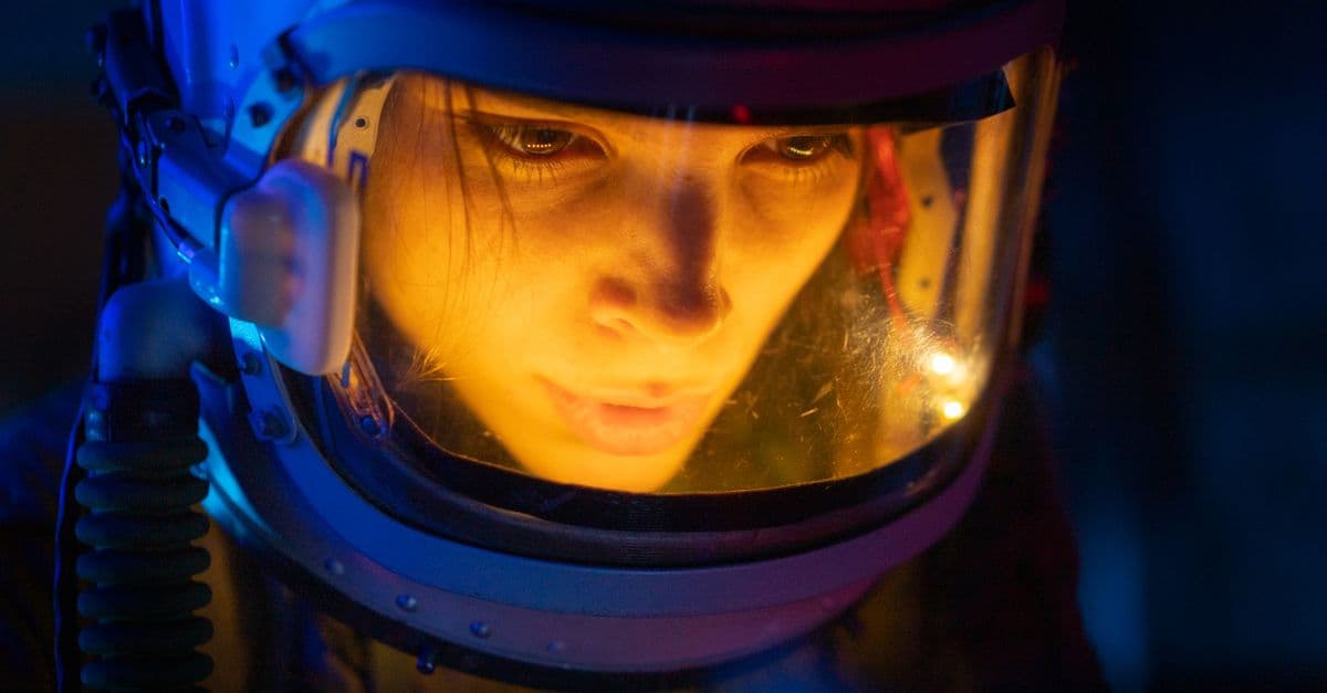 Close-up of a woman in a space suit under blue light, looking focused and futuristic.