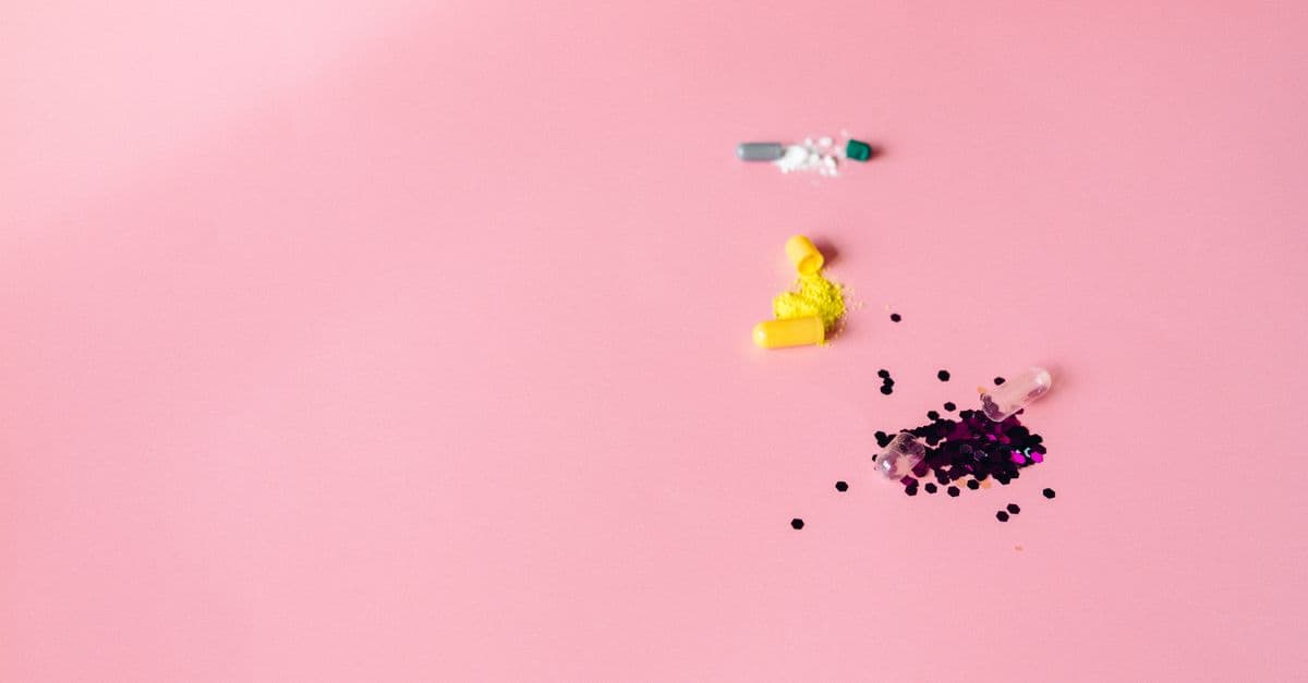 Close-up flat lay of colorful capsules and powders on pink surface with copy space.