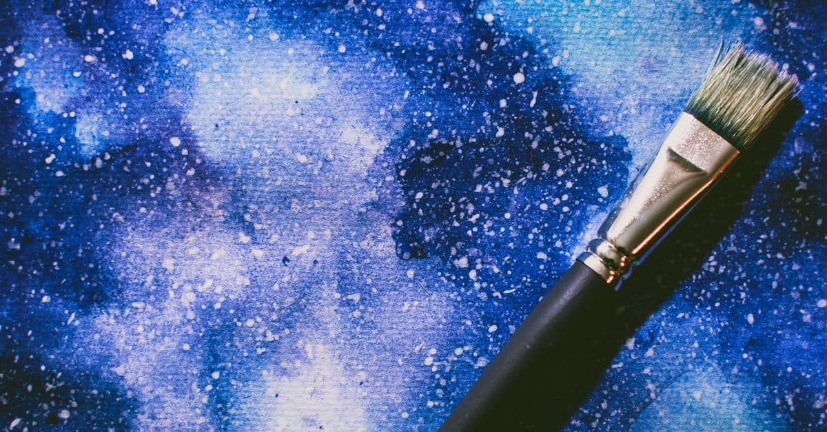 Vibrant abstract watercolor art with a paintbrush lying on a textured blue canvas.
