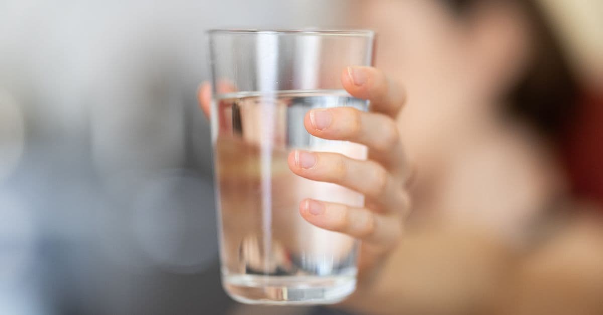 A hand holding a clear glass of water with a blurred background for health and hydration concept.