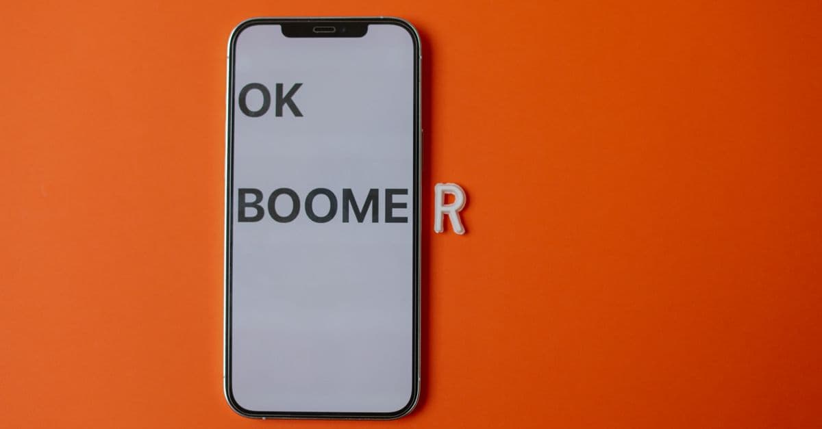 Modern smartphone displaying 'OK Boomer' on orange backdrop, symbolizing generational divide.