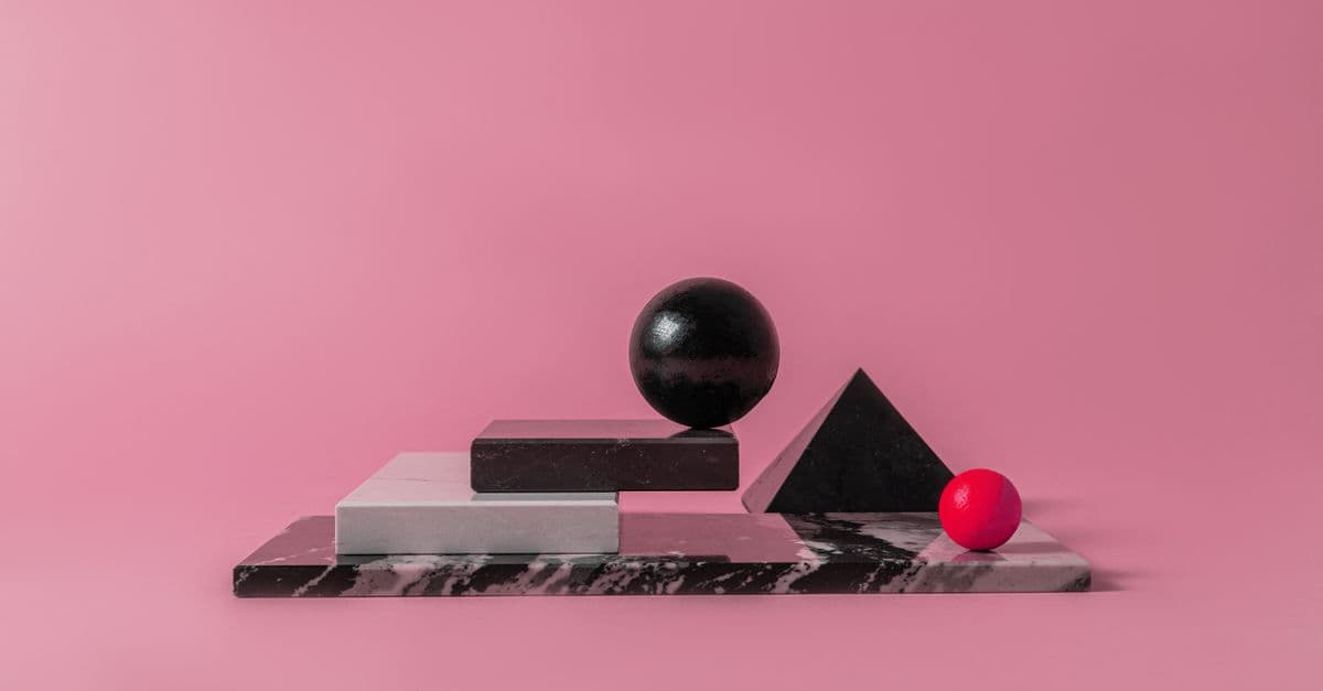 Minimalist arrangement of geometric shapes on a marble base with a pink backdrop.
