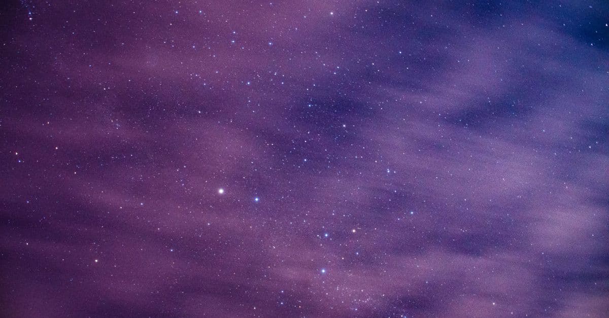 Long exposure of cosmic background with dark night sky with glowing bright stars behind light floating clouds