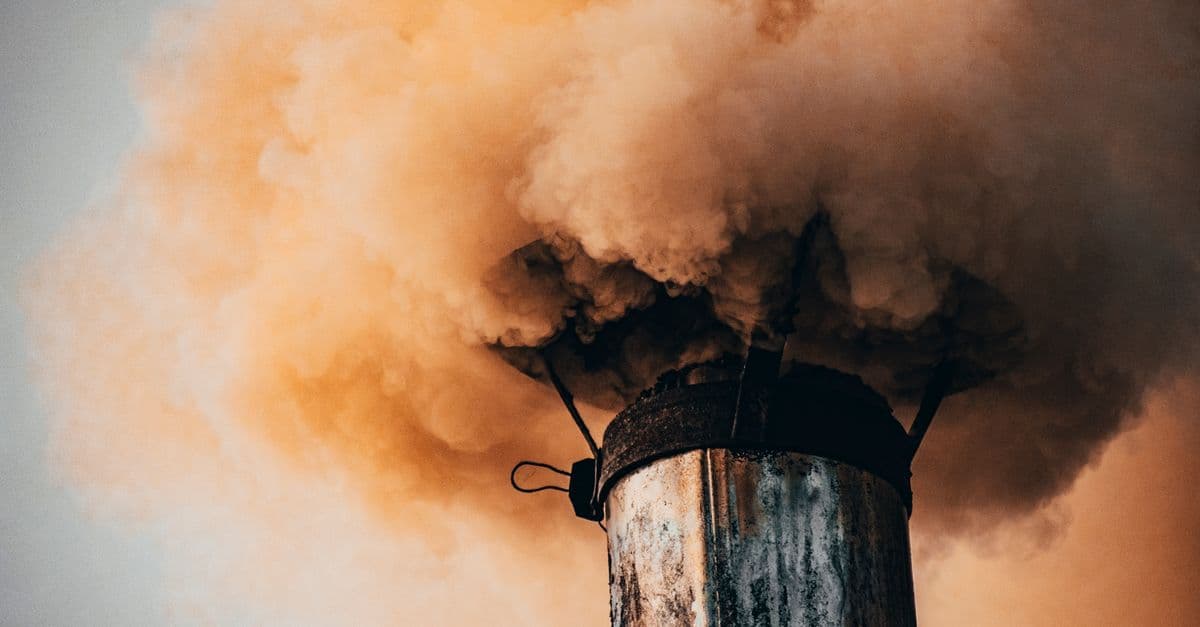 A close-up of a factory smokestack releasing thick smoke into the air, illustrating industrial pollution.