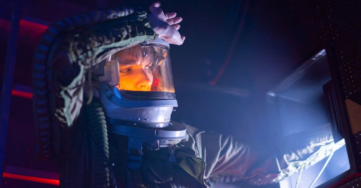 A woman in a spacesuit explores a futuristic spacecraft interior with dramatic lighting.