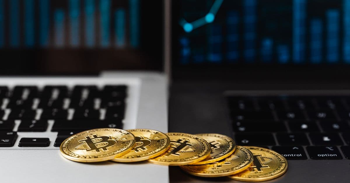 Gold bitcoins placed on laptop keyboards with digital financial graphs in the background.