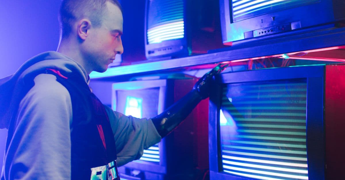 A man with a prosthetic arm interacts with vibrant vintage televisions in an industrial setting.