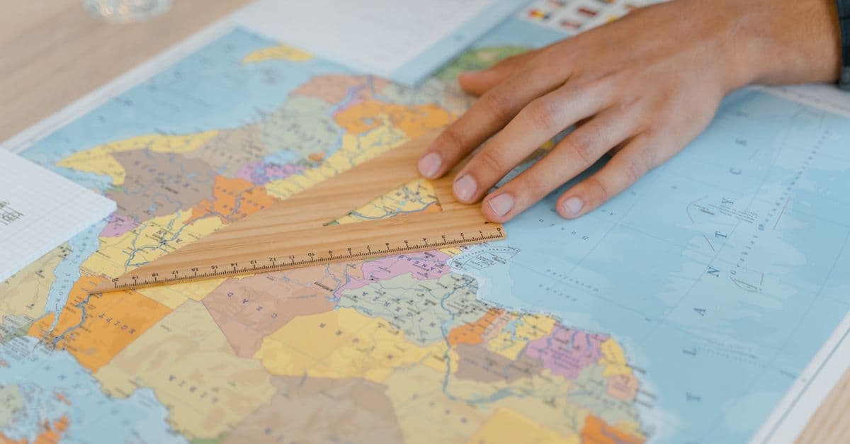 A hand uses a wooden ruler on a world map, focusing on precise measuring.