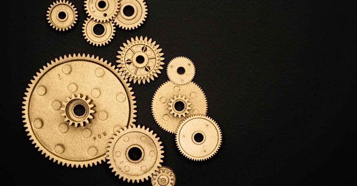 Close-up of gold gears arranged on a black backdrop, symbolizing teamwork and technology.