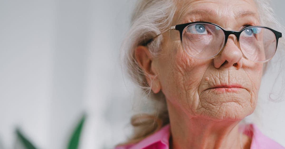Close-up portrait of a thoughtful elderly woman wearing glasses indoors.