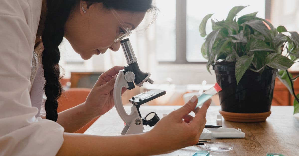 Woman examining sample under microscope in a lab, emphasizing research.