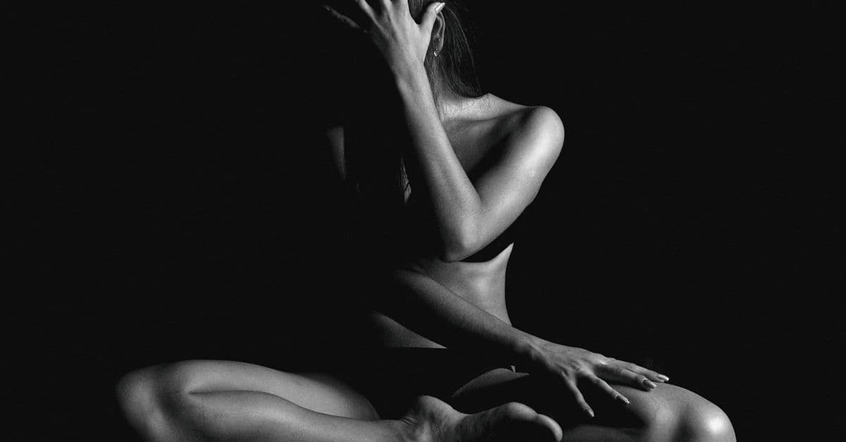 A dramatic black and white portrait of a woman sitting in a contemplative pose.