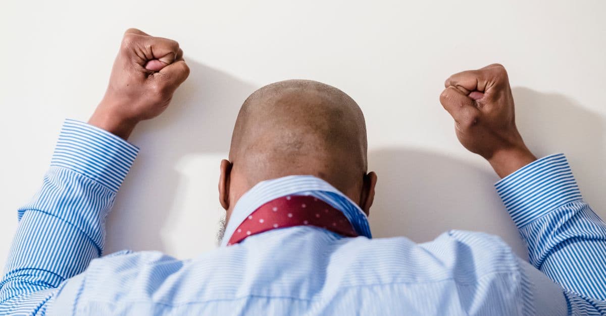 A bald man in a blue striped shirt with clenched fists expressing frustration against a white background.