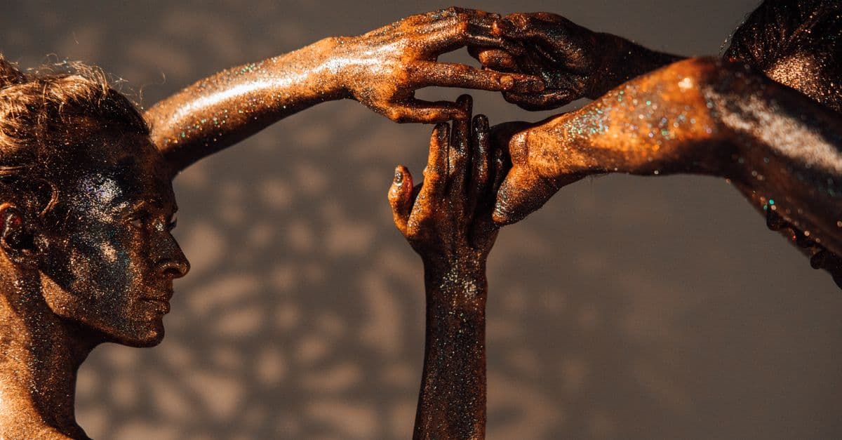 Close-up of people covered in glitter posing artistically with intertwined hands.