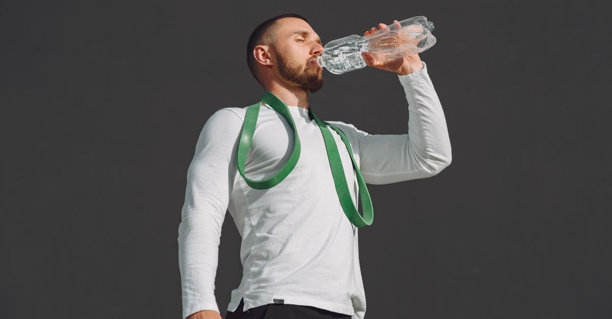 Athletic man in sportswear drinking water outdoors, promoting hydration.