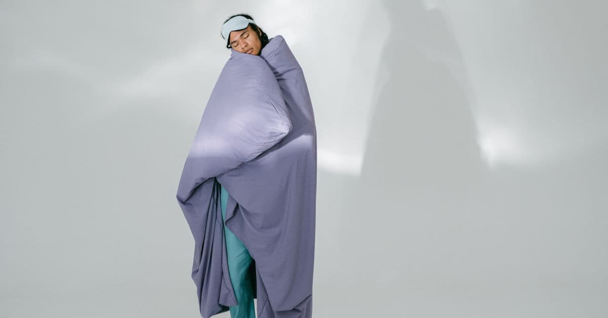 African American man wrapped in a purple blanket, wearing eye mask, resting in studio.