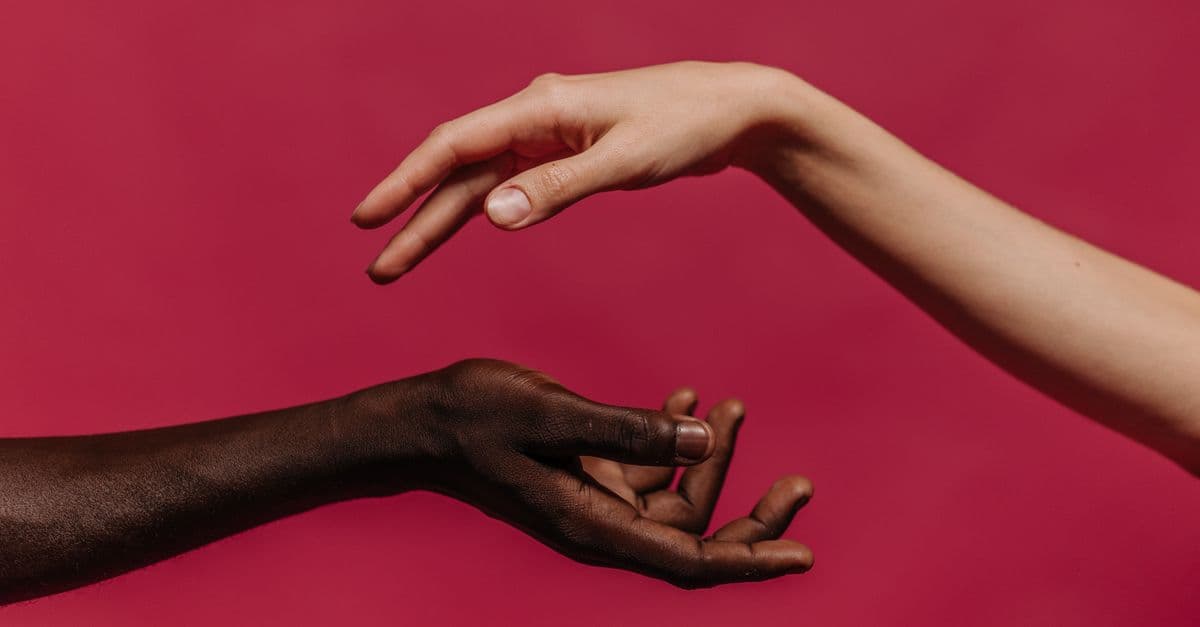 Two hands reaching towards each other against a vibrant pink background, symbolizing connection and diversity.