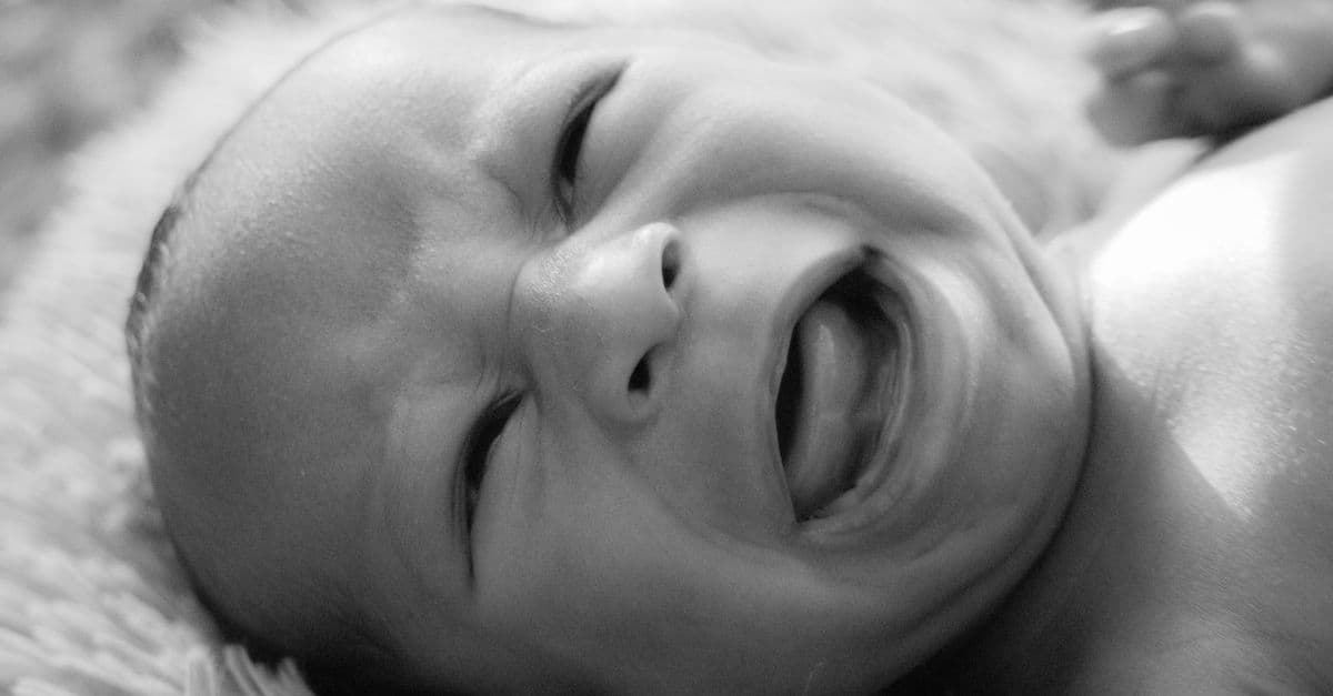Emotive black and white close-up of a crying newborn baby with strong emotional expression.