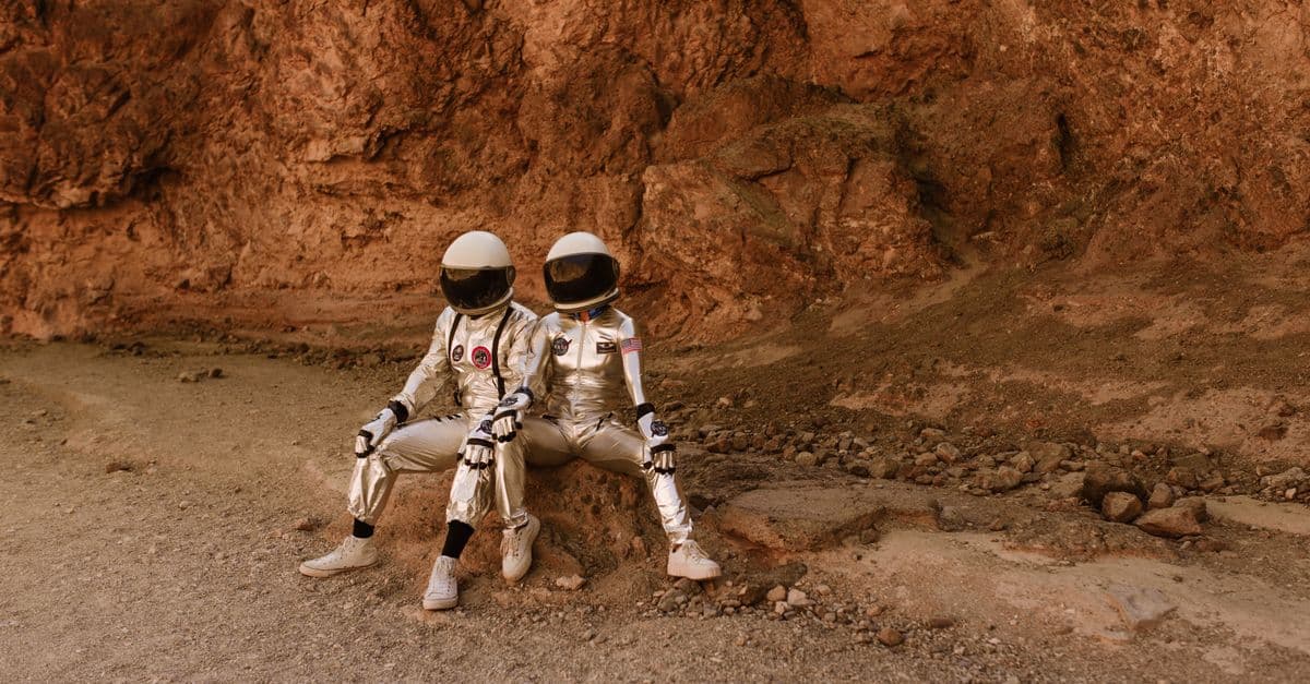 Two astronauts in space suits relax on rocky terrain resembling Mars, evoking exploration and adventure.