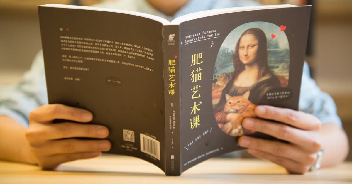 Person reading a book with 'Fat Cat Art' cover featuring Mona Lisa and a cat.