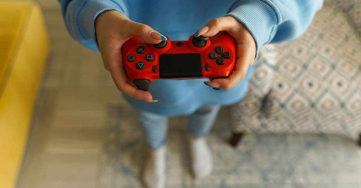 Person holding a bright red gaming controller indoors, focusing on gameplay.