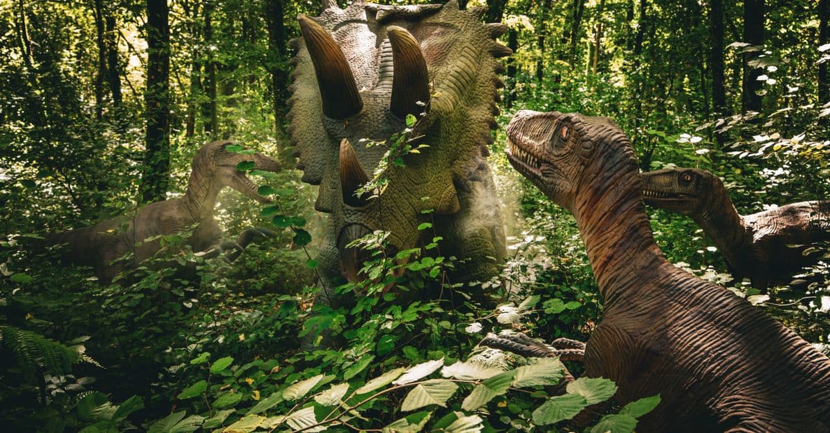 Realistic dinosaur models in a lush forest create an educational prehistoric scene.