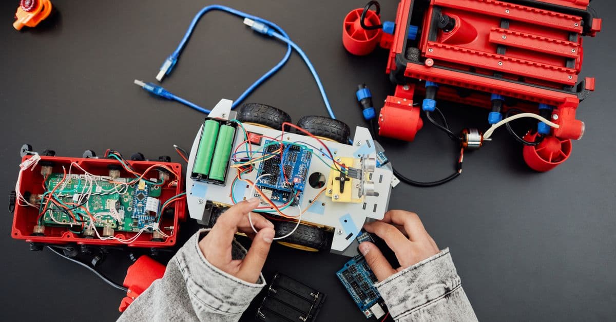 Young hands working on a robotics project with toy cars and circuits, focusing on innovation and education.