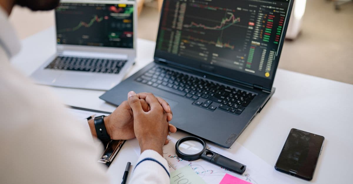 Business professional analyzing stock market data on dual laptops in an office.